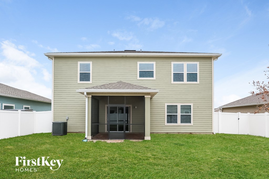 a beige house with a grass lawn and a white fence