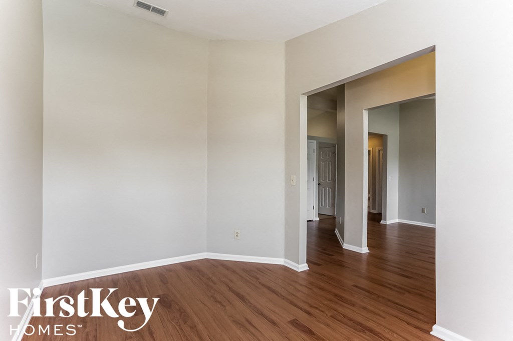 a living room with white walls and a wooden floor and a hallway with a door