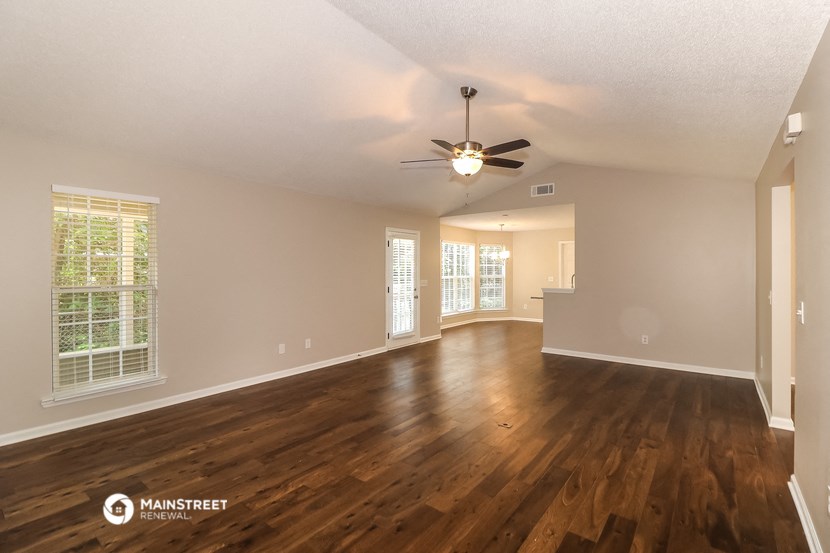 the spacious living room with hardwood flooring and a ceiling fan