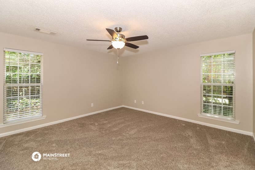 the spacious living room has a ceiling fan and two windows