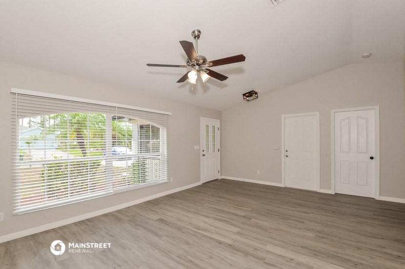 the spacious living room with ceiling fan and large window