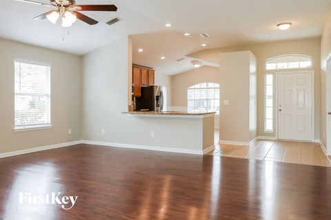 an empty living room with a kitchen and a ceiling fan