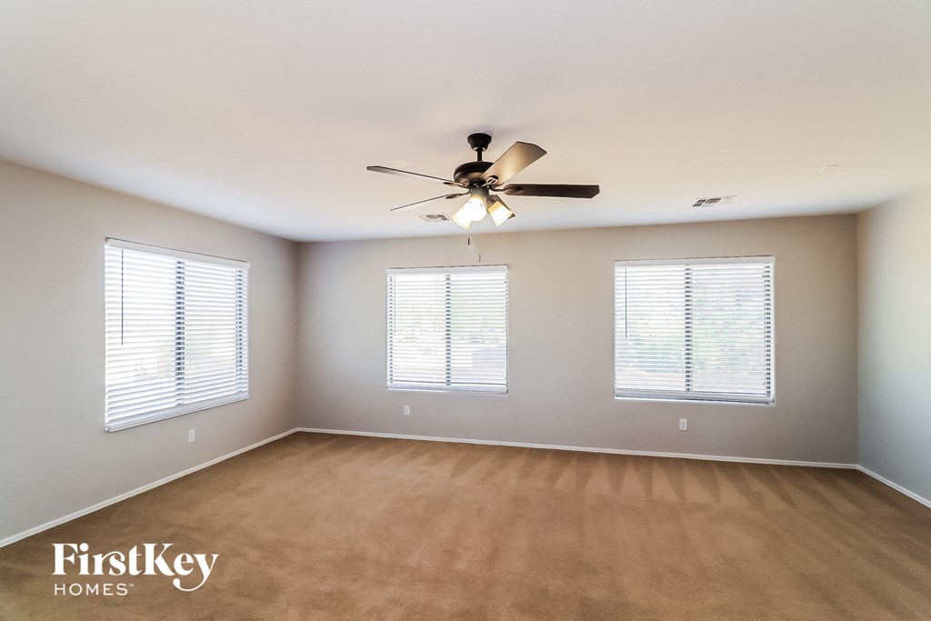 an empty living room with a ceiling fan and three windows