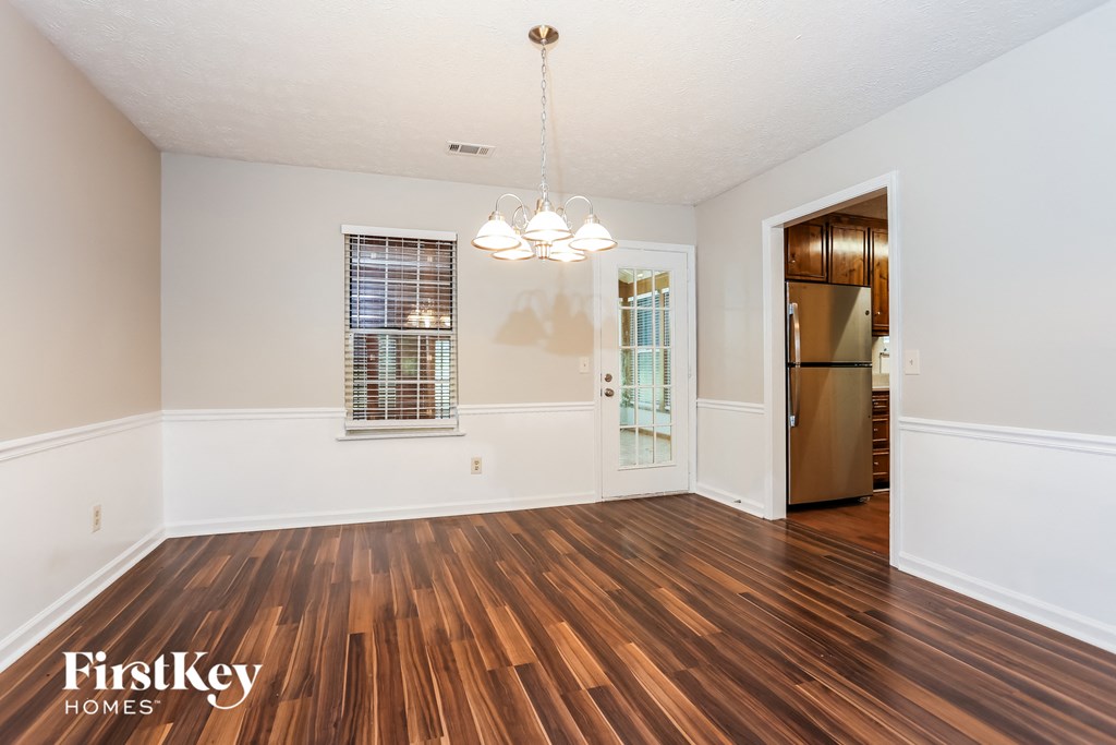 an empty living room with wood flooring and a door to the kitchen
