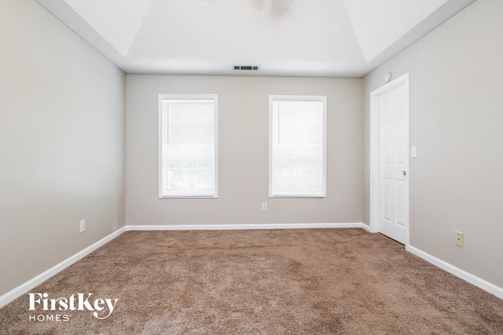 a carpeted room with two windows and a door