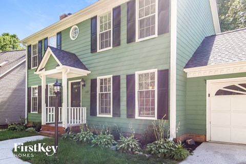 a green house with a white porch and a white garage door