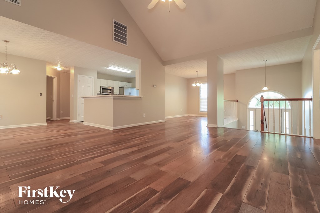 A spacious room with wooden flooring and a staircase on the right side.