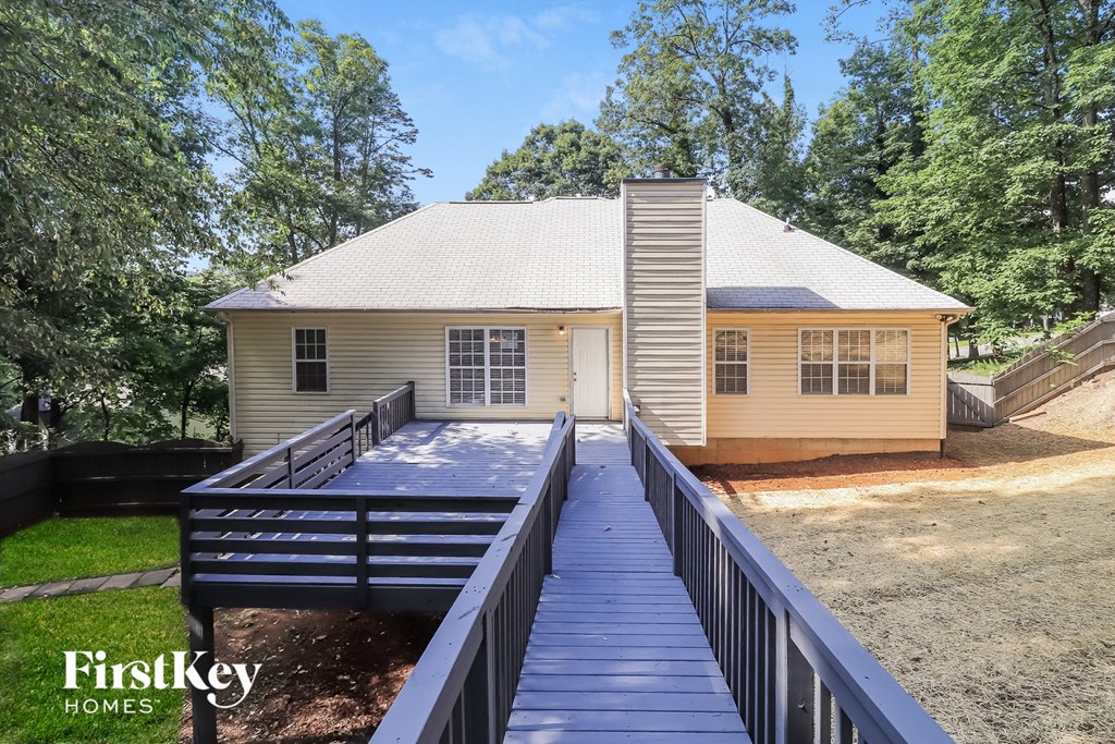 A house with a porch and a deck is surrounded by trees.