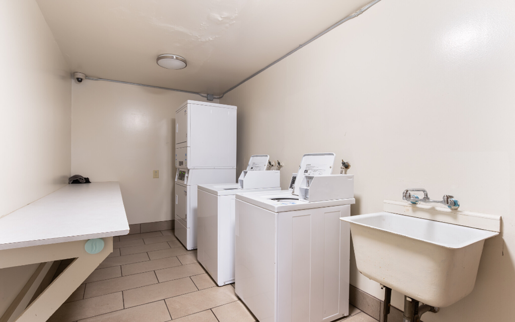 a laundry room with four washing machines and three sinks and a refrigerator