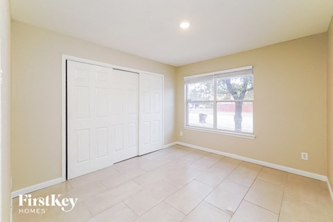 A room with a white door and a window with a view of a tree and a building outside.