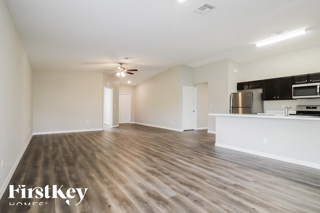 an empty living room with a kitchen and a ceiling fan