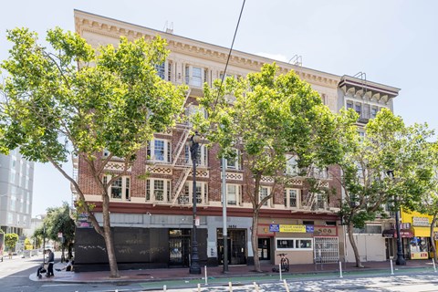 A large building with a balcony on the second floor is surrounded by trees.
