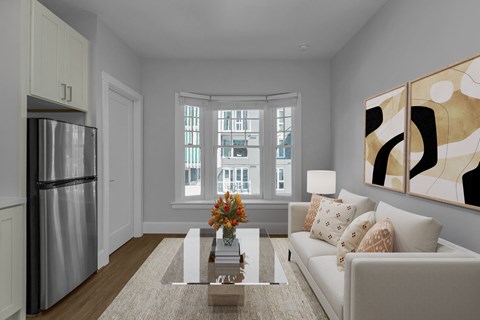 A modern living room with a stainless steel refrigerator, a coffee table with a vase of flowers, a couch with throw pillows, and a large abstract painting on the wall.