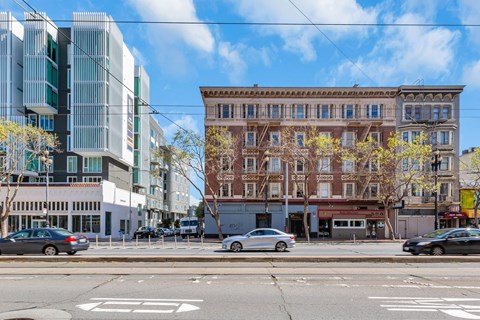 A street view with cars, a building with a red awning, and a tree with yellow leaves.