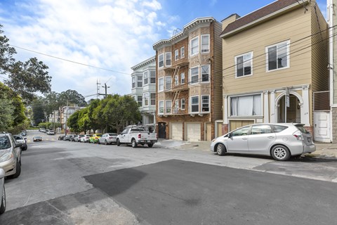 A street view with cars parked on the side and buildings in the background.