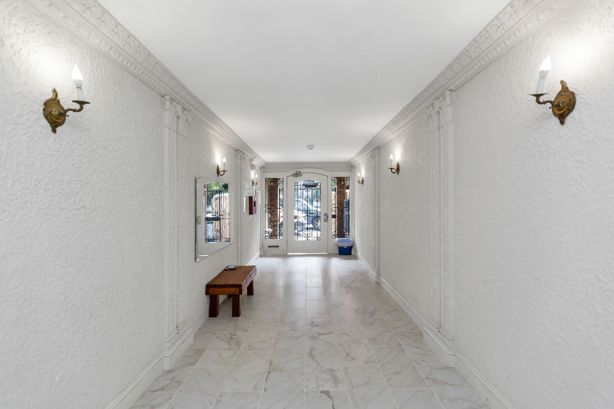 A long white hallway with a bench and wall sconces.