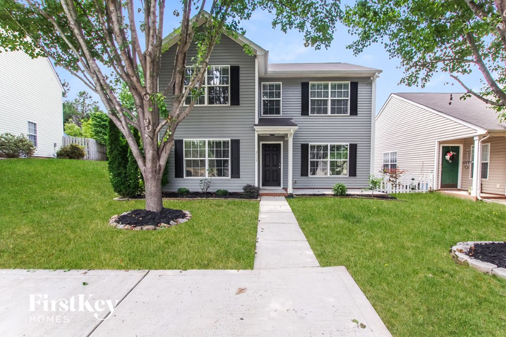 A grey house with a tree in front of it.