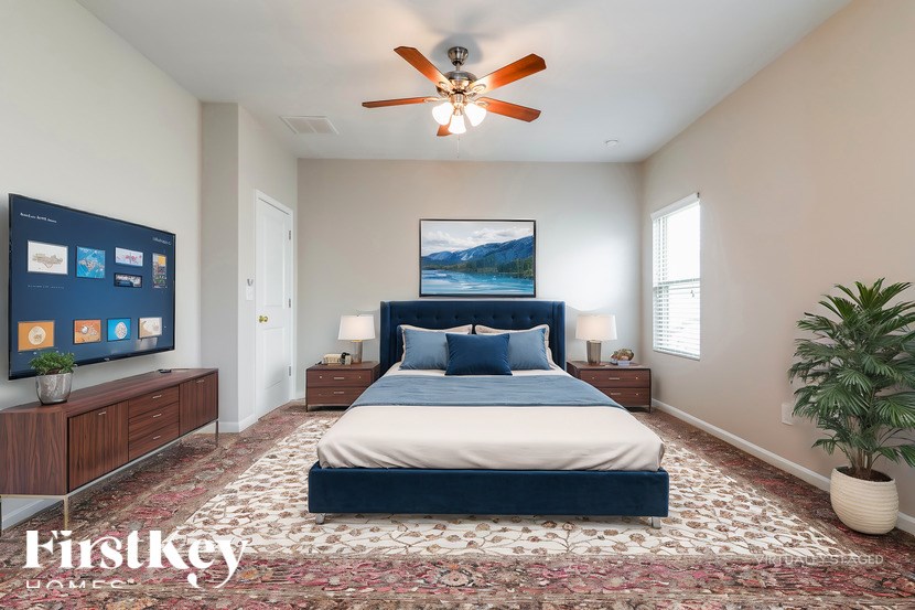 A bedroom with a large bed, a ceiling fan, and a television on the wall.