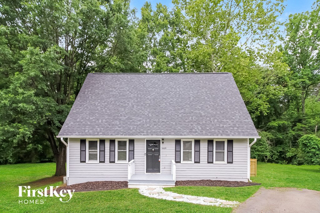 a small white house with a gray roof and trees