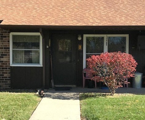 a front door of a house with a bench and a red tree
