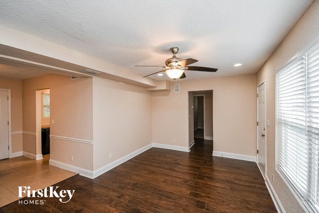 an empty living room with a ceiling fan and a door to a hallway