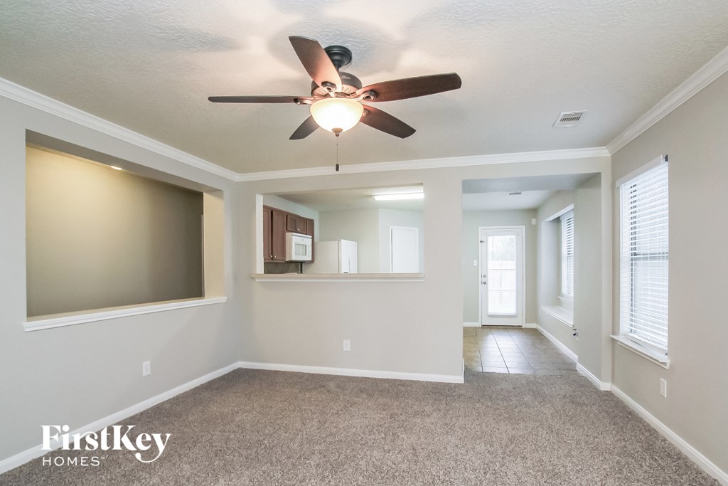an empty living room with a ceiling fan and a kitchen