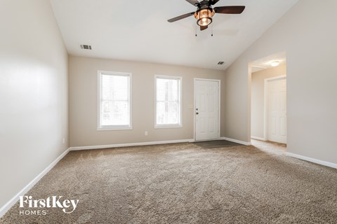 a spacious living room with carpet and a ceiling fan