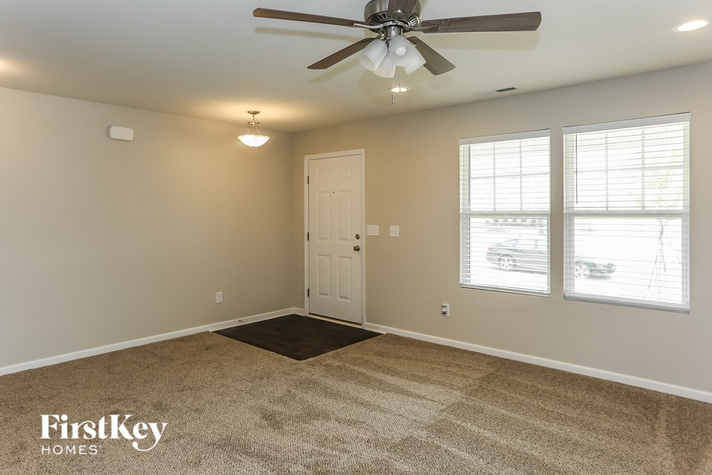 A room with a carpet, a ceiling fan, and a door.