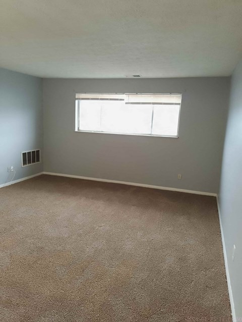 A room with a carpeted floor and a window with blinds.