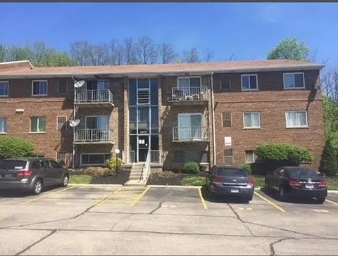 A parking lot in front of a brick apartment building with cars parked.