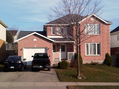 A red brick house with a black truck and a white car parked in front.