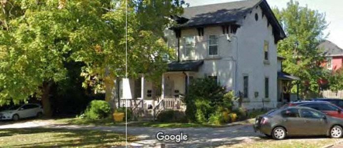 A white house with a black roof and a tree in front of it.