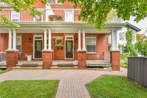 the front of a brick house with a porch and a lawn
