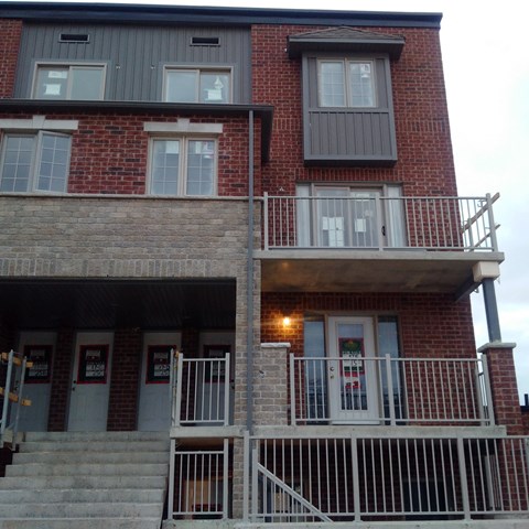 A red brick building with a balcony and stairs leading to the front door.