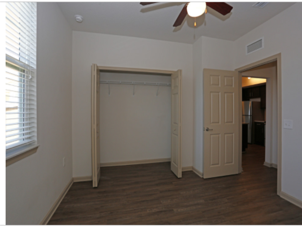 an empty living room with a ceiling fan and a closet