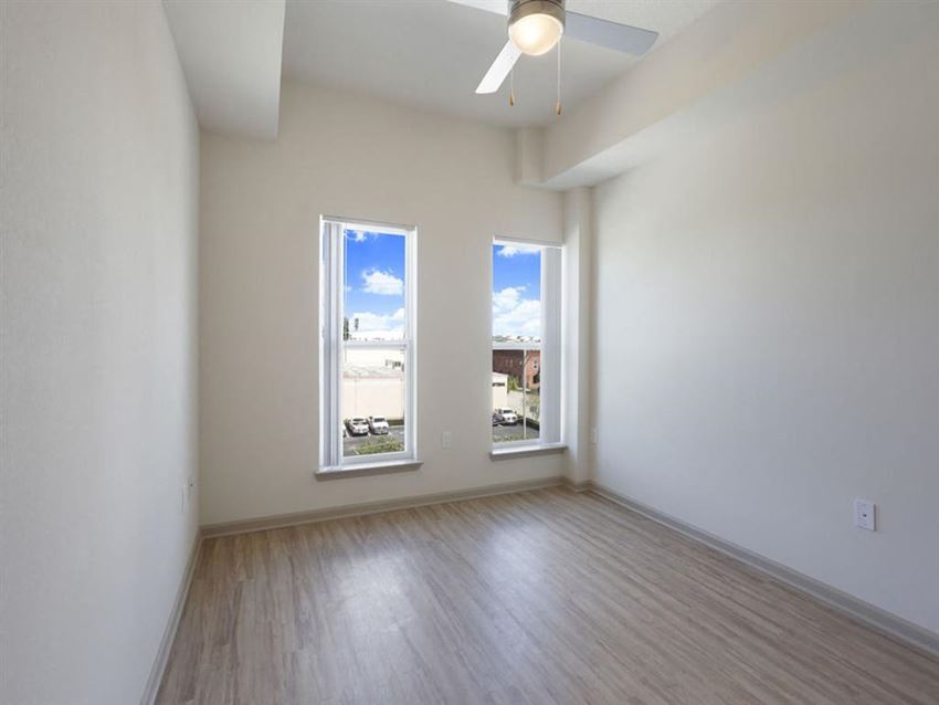 an empty living room with two windows and wood floors
