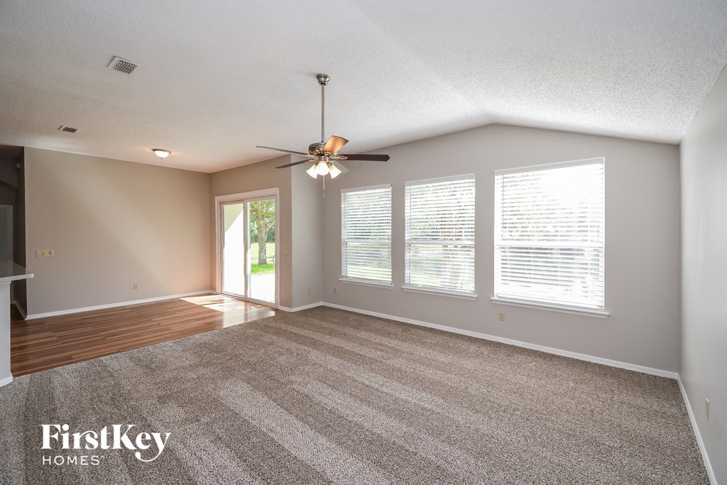 an empty living room with a ceiling fan and windows