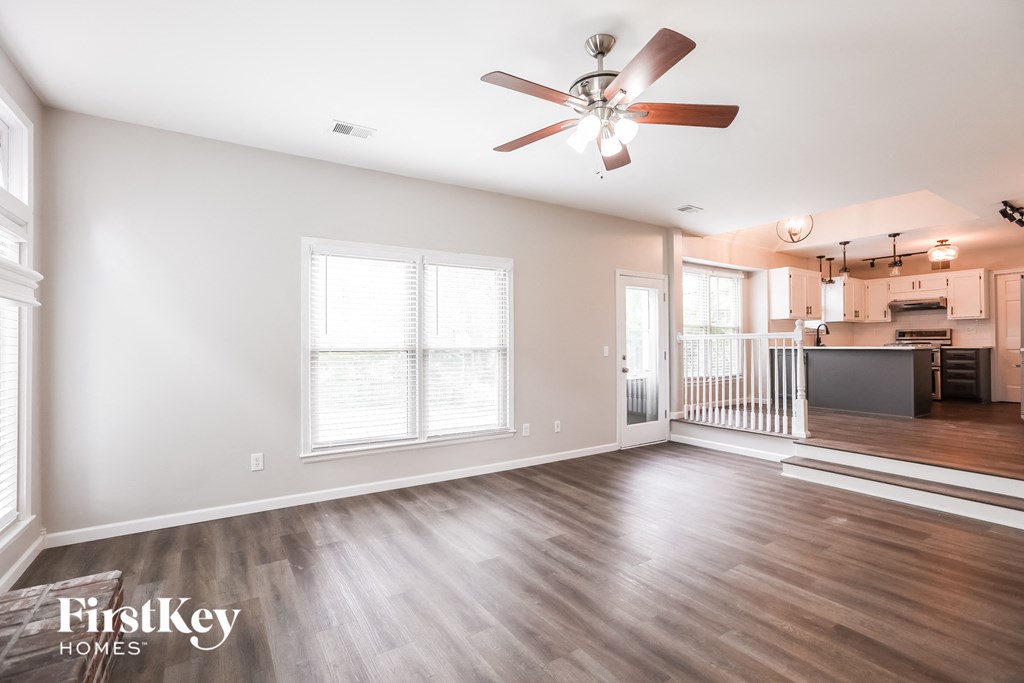 an empty living room with a ceiling fan and a kitchen