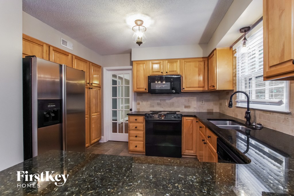 a kitchen with wooden cabinets and black countertops and a stainless steel refrigerator