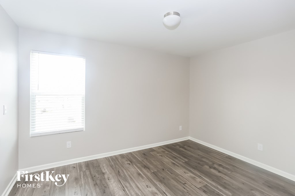a bedroom with white walls and wood floors and a window