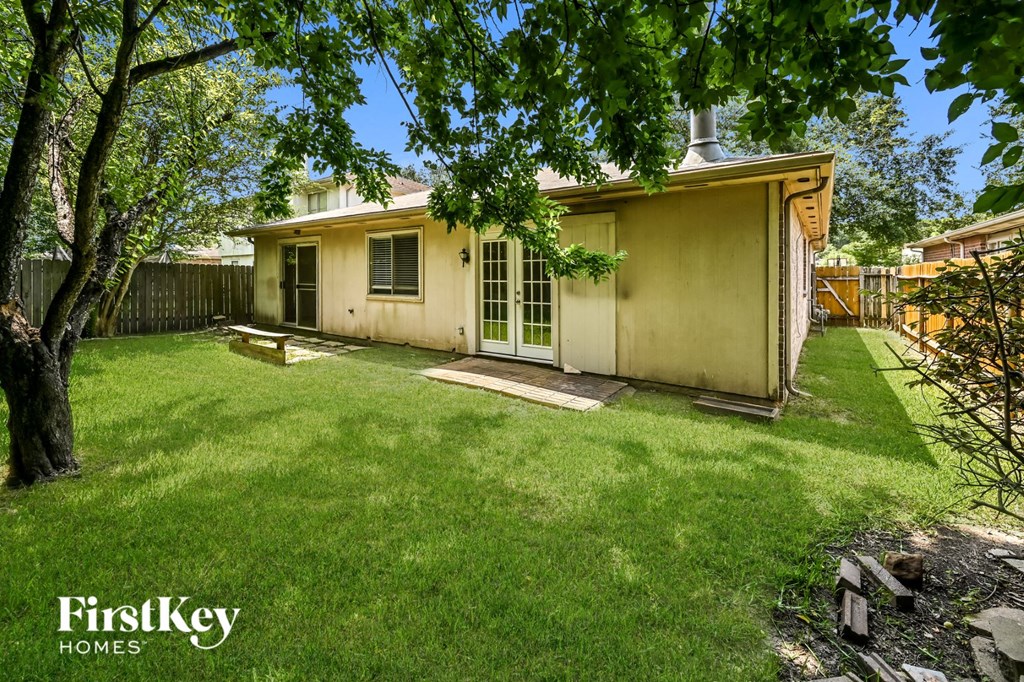 a backyard with a small yellow house and a tree