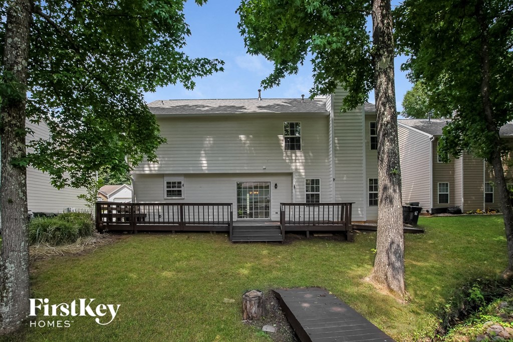 the back of a white house with a yard and a bench