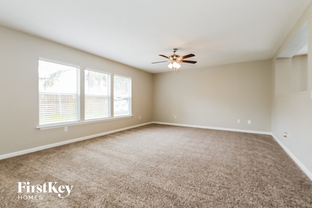 an empty living room with a ceiling fan and large windows