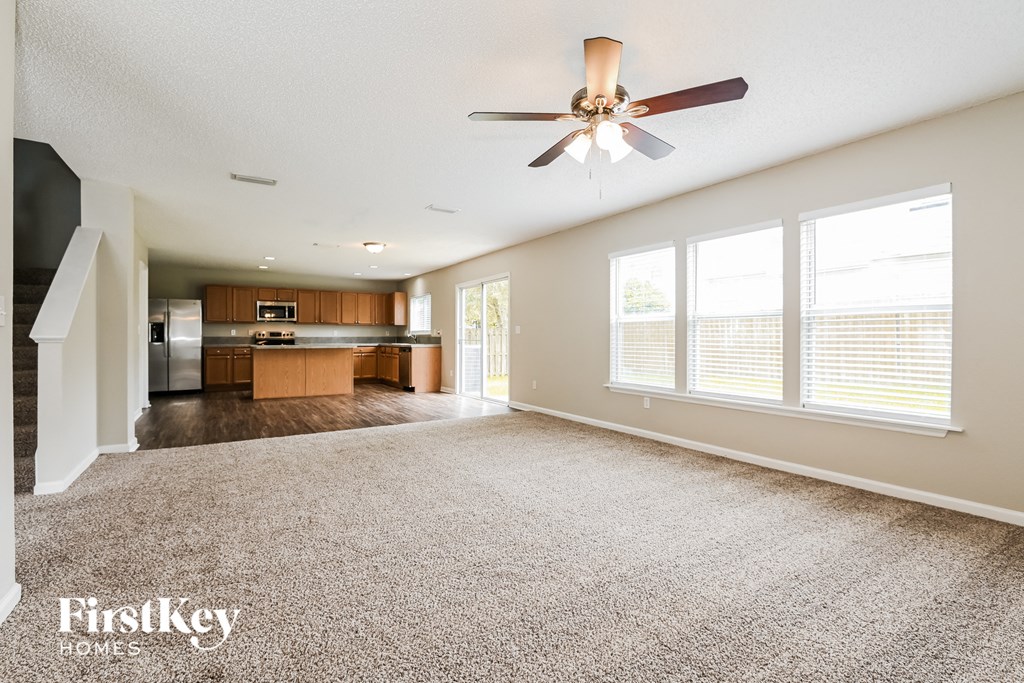 an empty living room with a ceiling fan and a kitchen