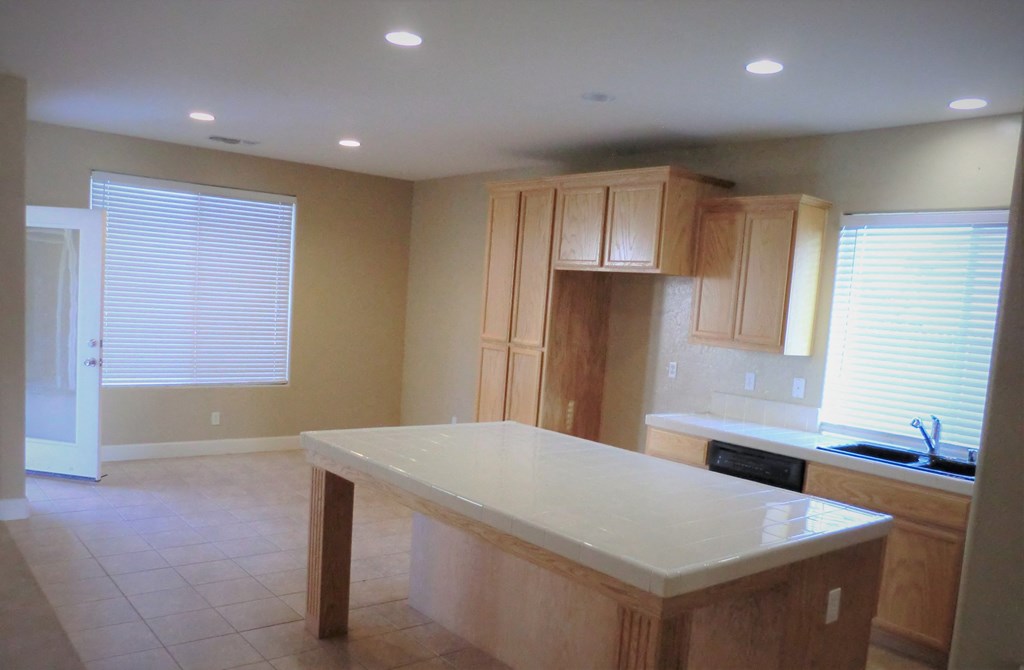 an empty kitchen with a white counter top and wooden cabinets