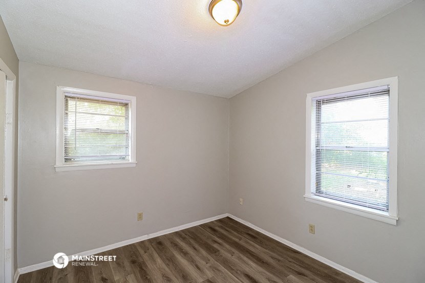 the bedroom of a rental home with wood flooring and two windows