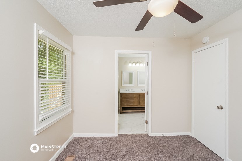 a bedroom with a ceiling fan and a door to a bathroom