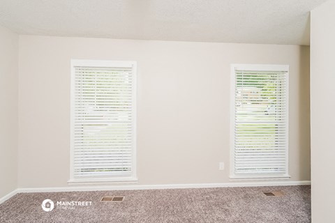 a living room with two windows with blinds and carpet