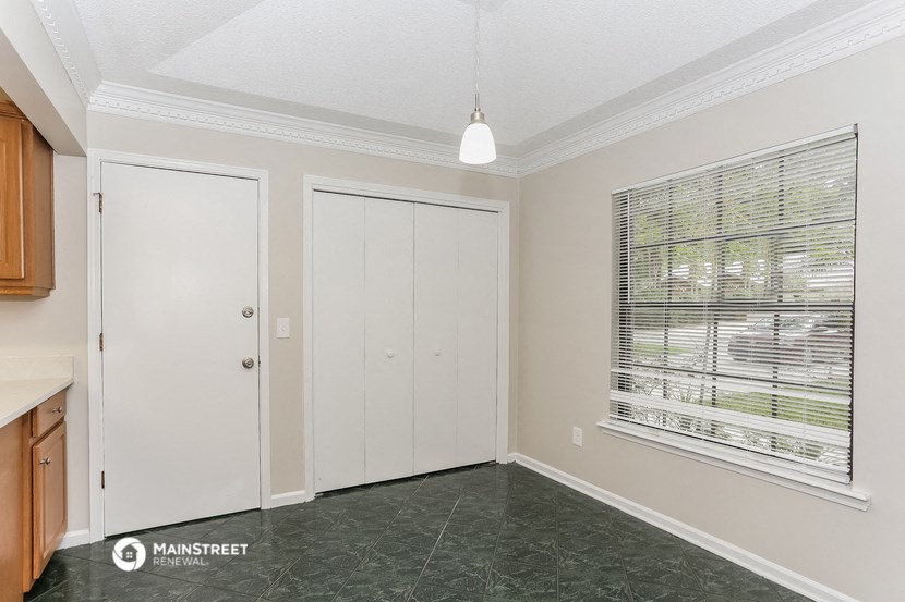 the living room of an apartment with a large window and a door to the kitchen
