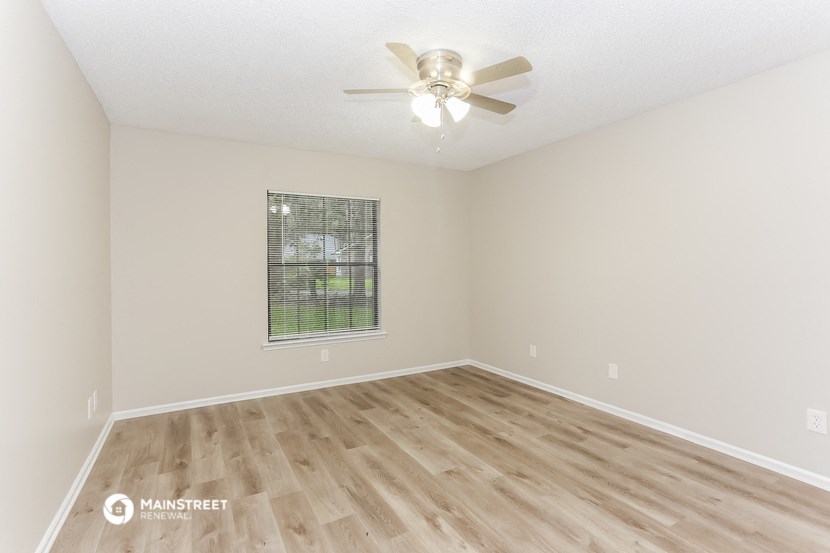 the spacious living room with hardwood flooring and a ceiling fan